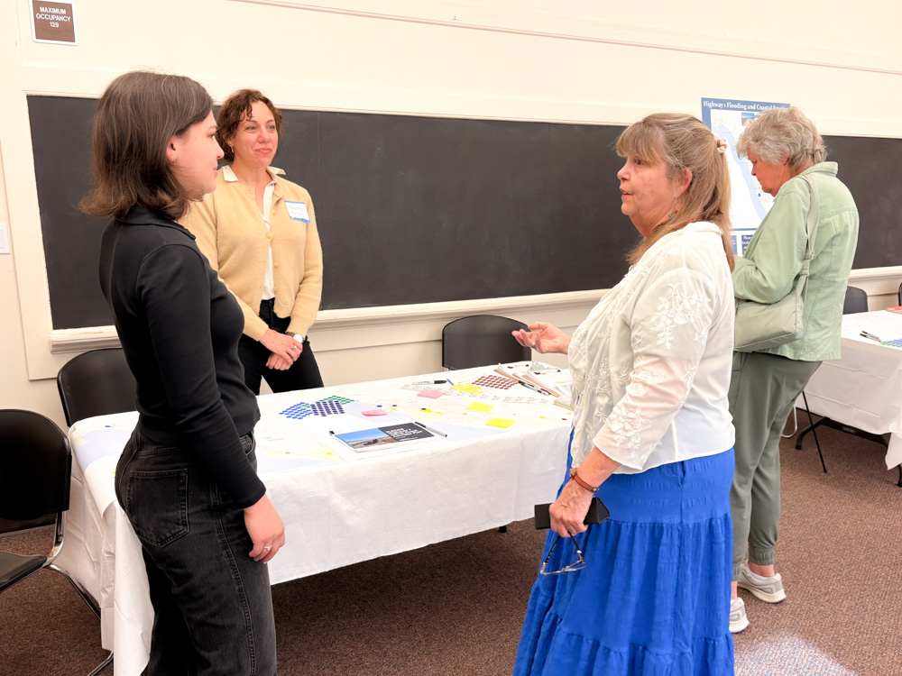 A group of community members and staff gather inside a brightly lit room at the Coast Unified School District for a Visioning Workshop, chatting in small groups and viewing information boards set up on easels.