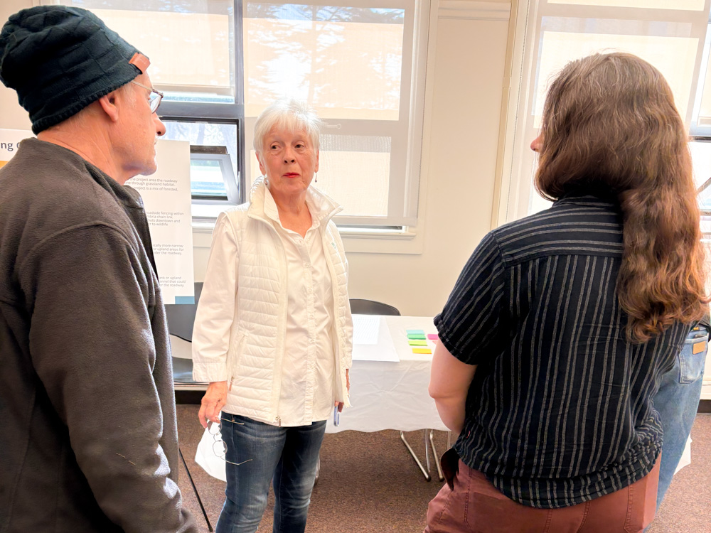 A group of community members and staff gather inside a brightly lit room at the Coast Unified School District for a Visioning Workshop, chatting in small groups and viewing information boards set up on easels.